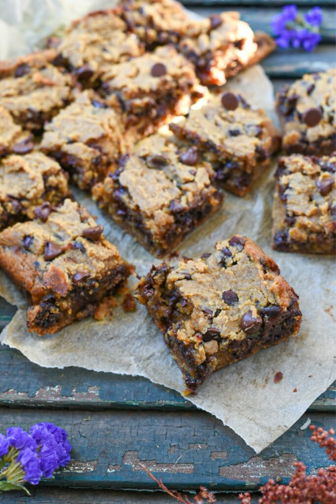 A bunch of chickpea blondie squares on parchment paper over a blue rustic wooden surface