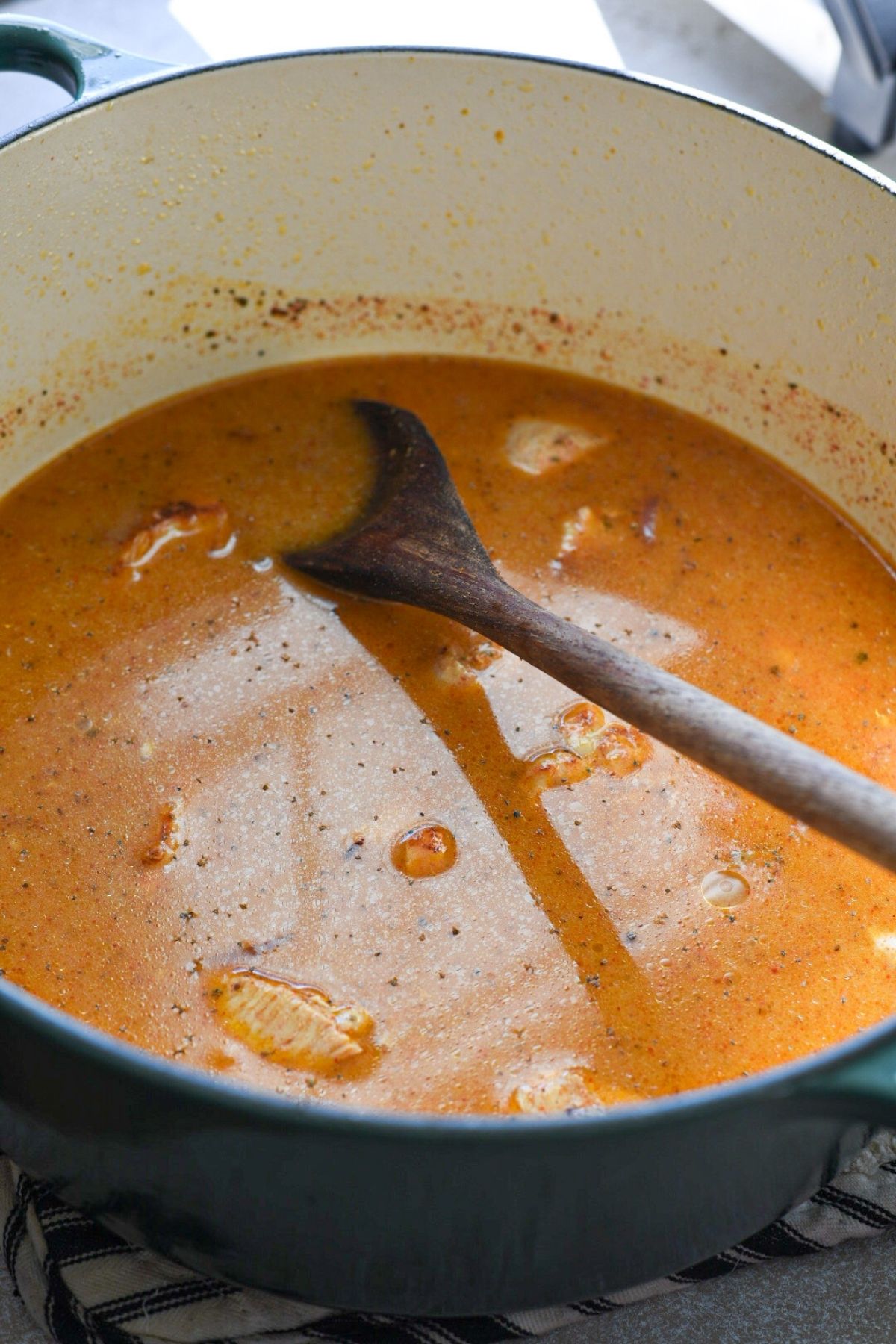 A large blue dutch oven filled with an orange broth, with pieces of chicken showing.