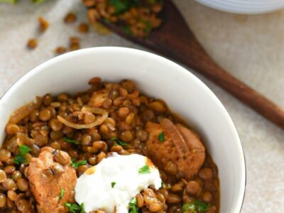 A small bowl filled with brown lentil stew, with pieces of cooked marinated chicken, yogurt and parsley on top