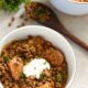A small bowl filled with brown lentil stew, with pieces of cooked marinated chicken, yogurt and parsley on top