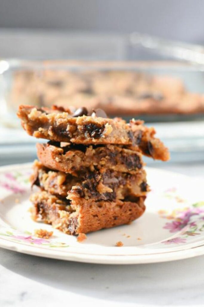 A straight shot of a stack of vegan chickpea blondie bars placed on a vintage tea cup plate with a blurred background.