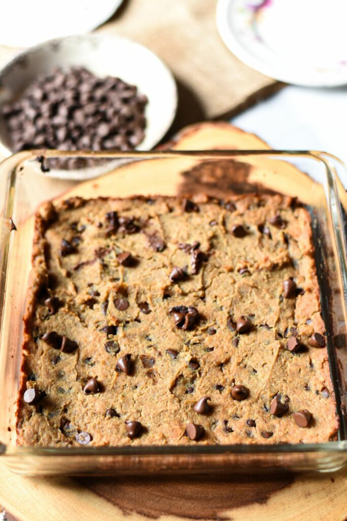 Cooked vegan chickpea blondies uncut in a glass baking dish sprinkled with chocolate chips.