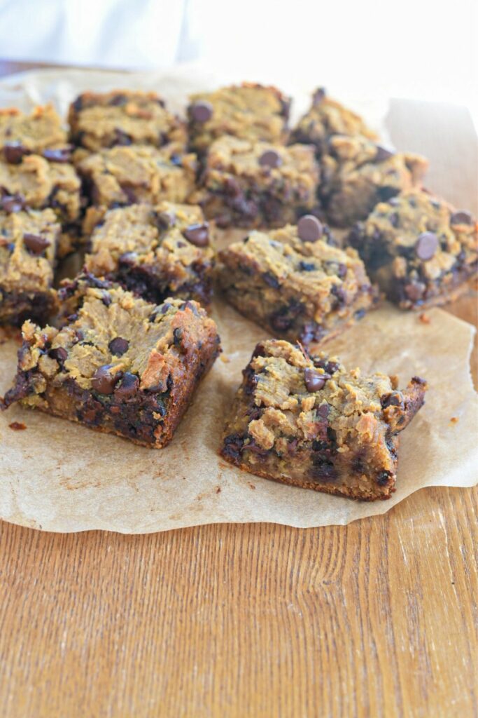 Close up shot of a bunch of vegan chickpea blondies on parchment paper over a light brown table