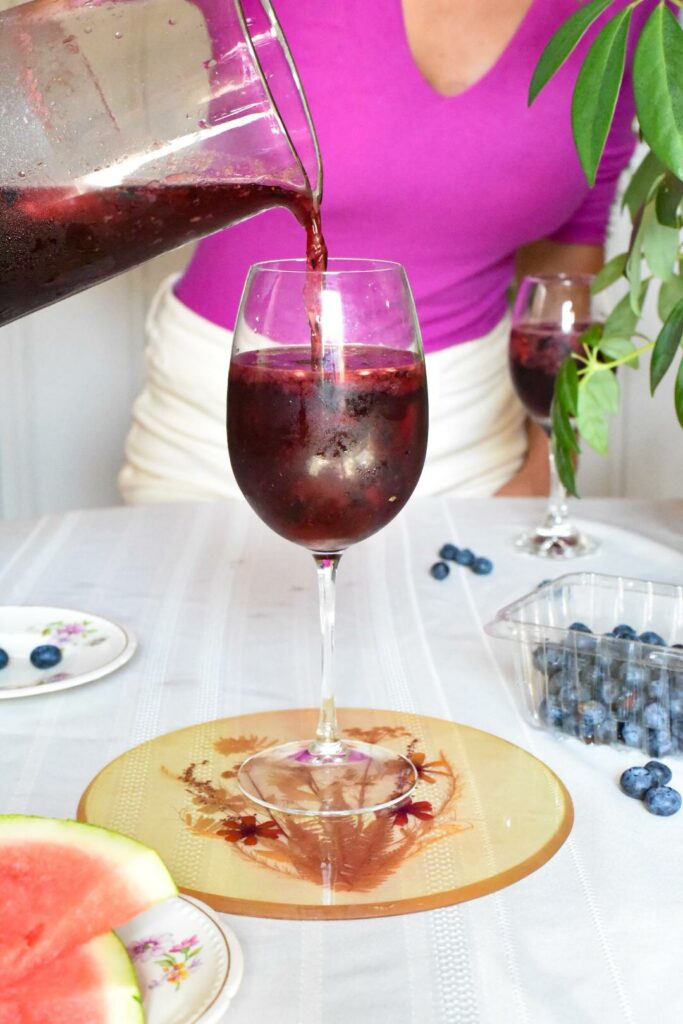 A wine glass being filled with a wine spritzer by a female in a pink shirt