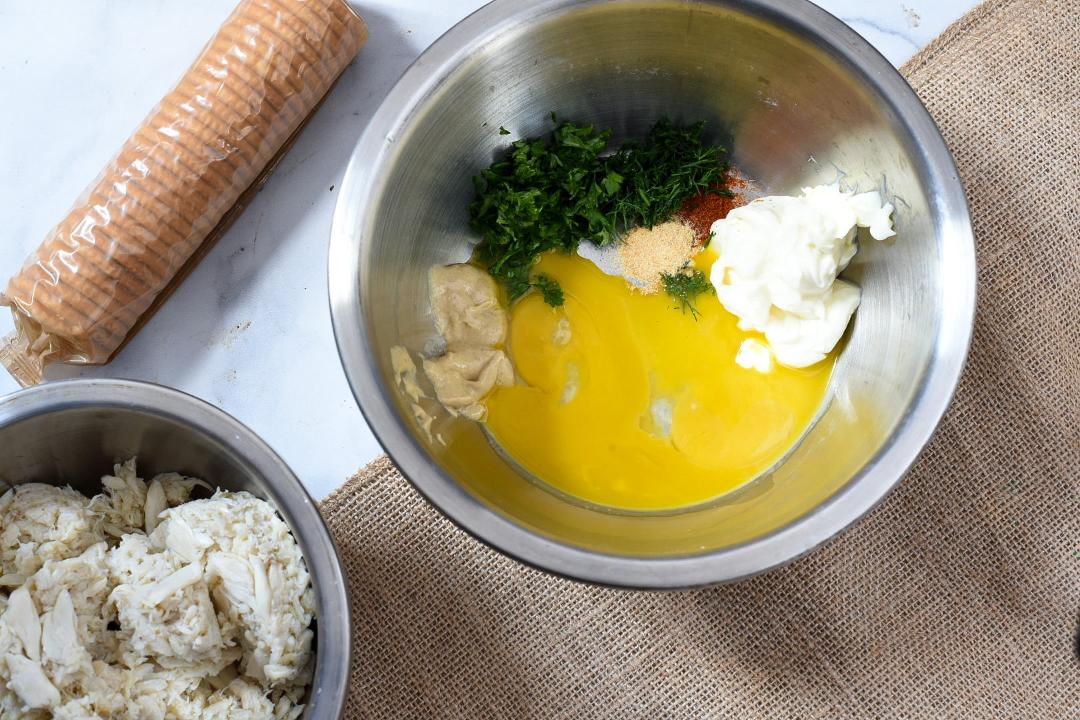 overhead shot of ingredients in a bowl, including yellow yolk and parsley, and a sleeve of ritz crackers can be seen in the corner
