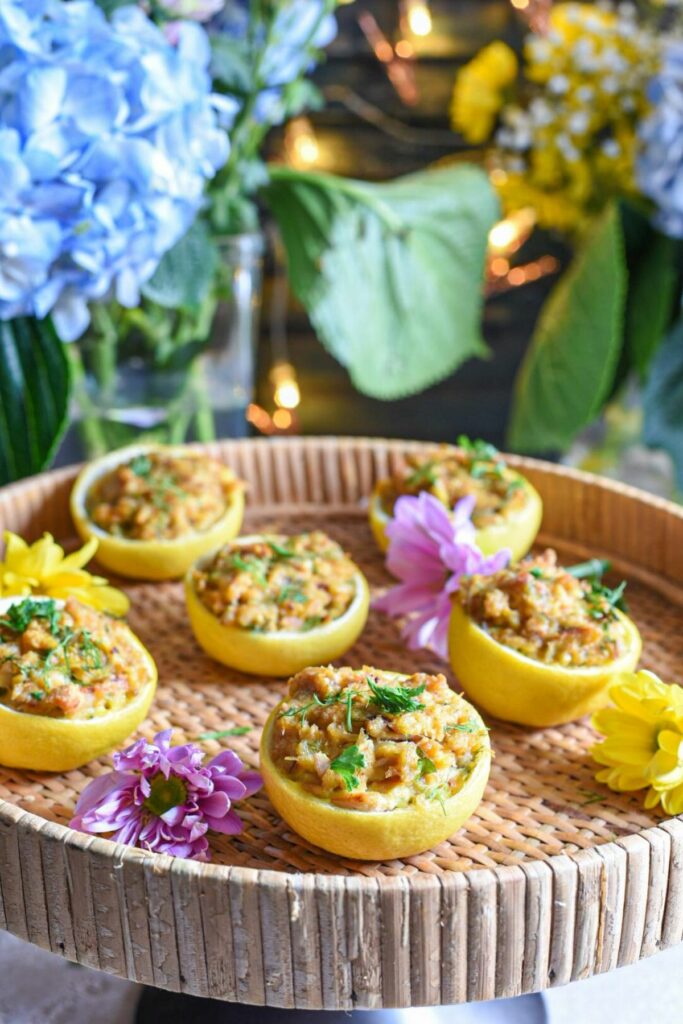 A wicker serving tray filled with Lemon stuffed crab cakes, with blue and purple flowers in the background