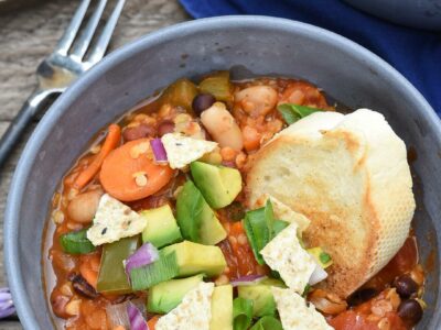 Rustic bowl of the ultimate vegan chili with carrots, lentils, beans, avocado and red onion.
