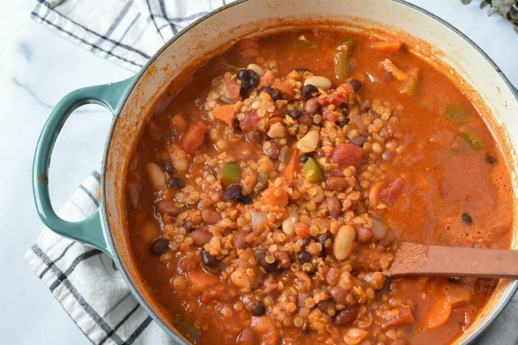 A large teal dutch oven filled with easy vegan chili with beans, lentils and green bell pepper on top.