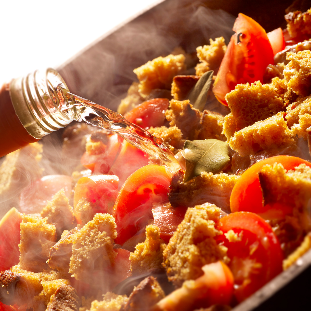 A wine bottle deglazing a pan filled with tomatoes and herbs.