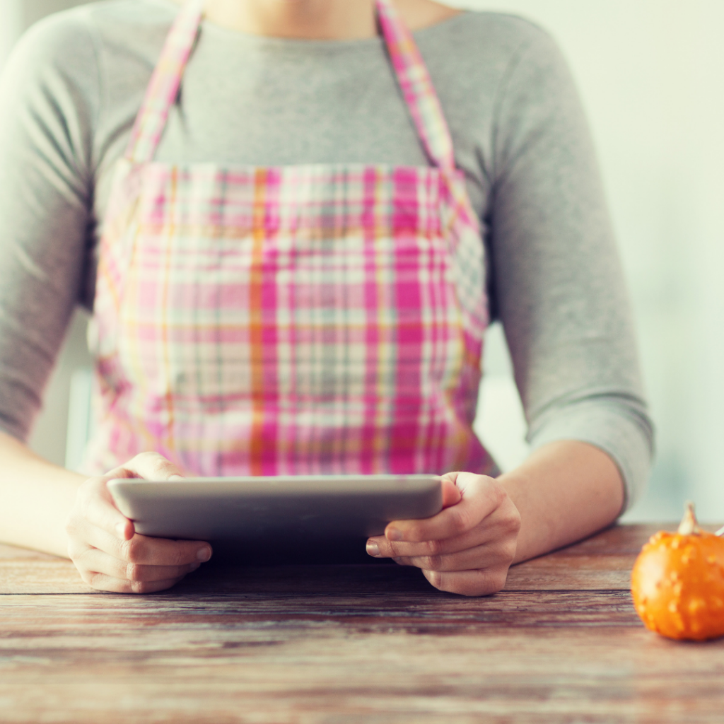 A woman wearing a pink apron reading a recipe from a tablet