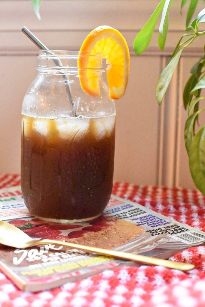 A large mason jar filled with an orange coffee drink with an orange slice on the rim