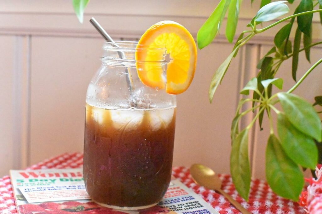 A large glass mason jar with a metal straw and orange coffee tonic inside.