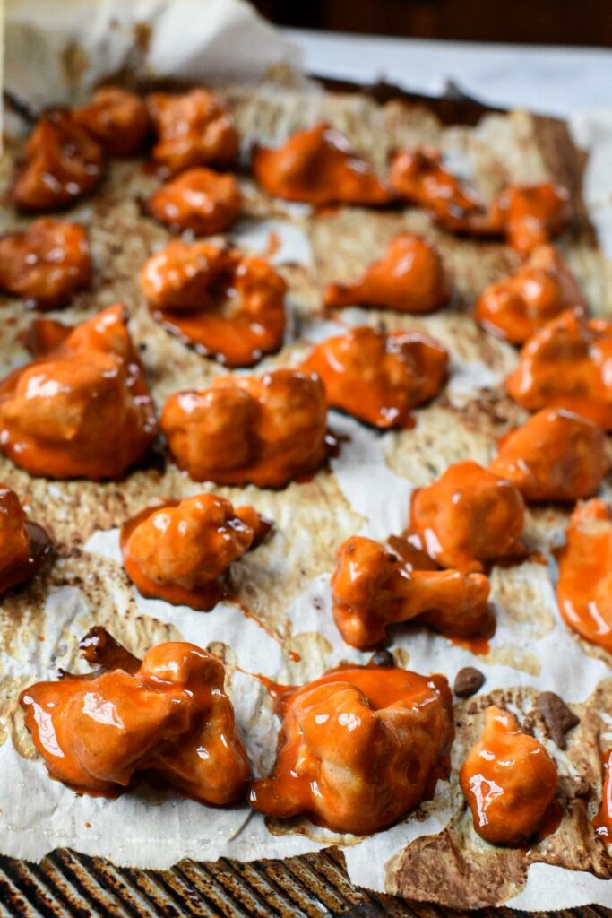 Baked buffalo cauliflower wings recently dipped in bright red wet buffalo sauce on a baking sheet lined with parchment paper.