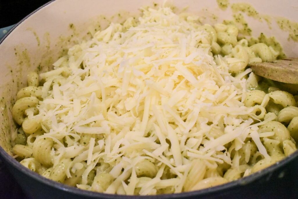 Shredded cheese over a large pot of healthy zucchini mac n cheese.