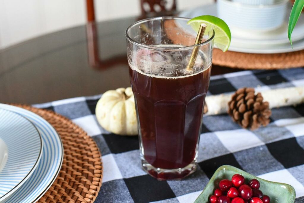 A cranberry lime coffee tonic in a large glass with a gold straw and slice of lime on a black and white table cloth.