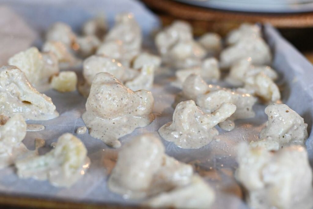 A close image of battered cauliflower wings on a parchment paper lined baking sheet