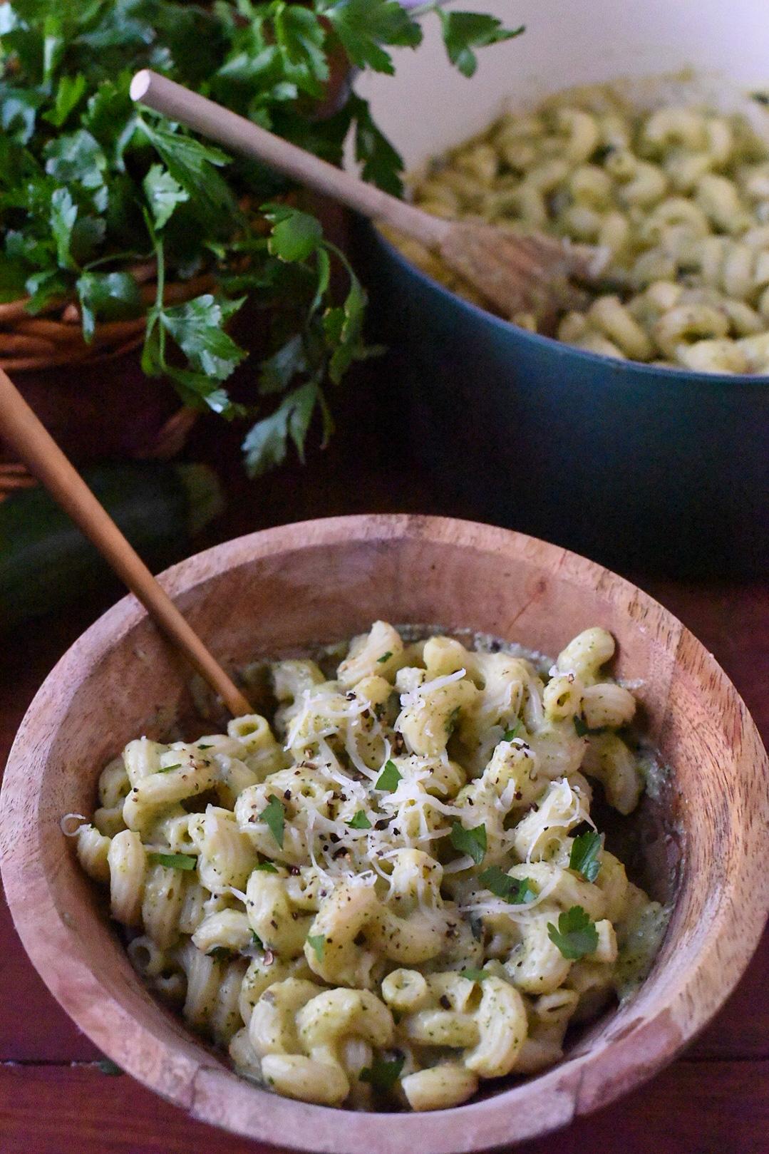 A wooden bowl filled with easy zucchini mac and cheese, topped with parsley and fresh cracked black pepper.