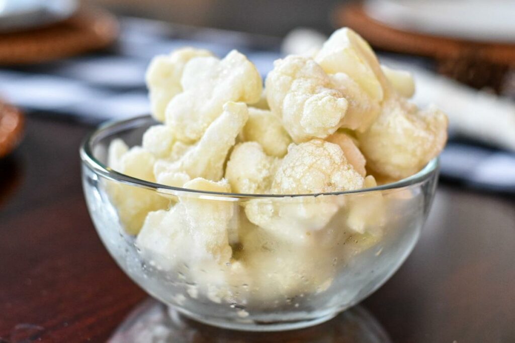 A very close image of a glass bowl filled with frozen cauliflower florets