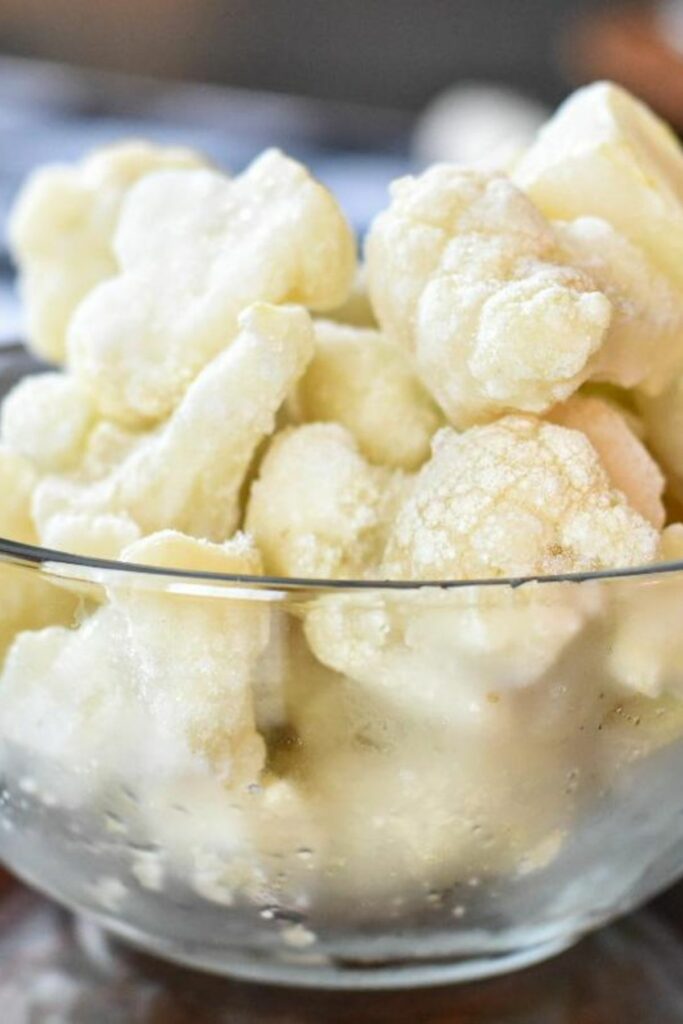 A close up shot of a glass bowl filled with frozen cauliflower florets