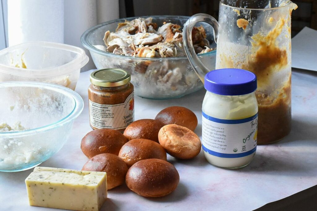 A counter filled with leftover Thanksgiving turkey, dinner rolls, mustard, cheese, gravy and mayonnaise.