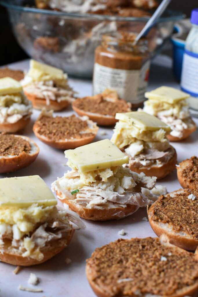 An assembly line of turkey sandwiches on a counter top, with 4 sandwiches open faced with turkey, mashed potatoes and cheese on top of them.