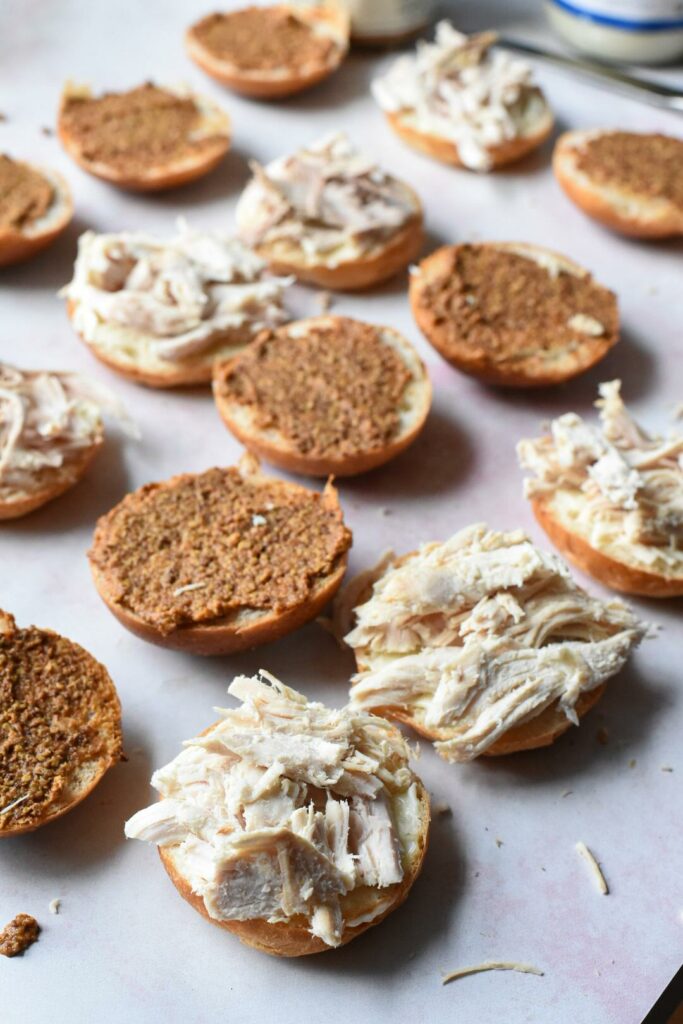 Turkey sliders being made with shredded turkey on the bottoms of the sandwiches and grainy mustard on the tops.