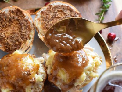 A gold spoon pouring gravy over turkey sliders on a gold rimmed plate.