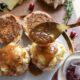 A gold spoon pouring gravy over turkey sliders on a gold rimmed plate.