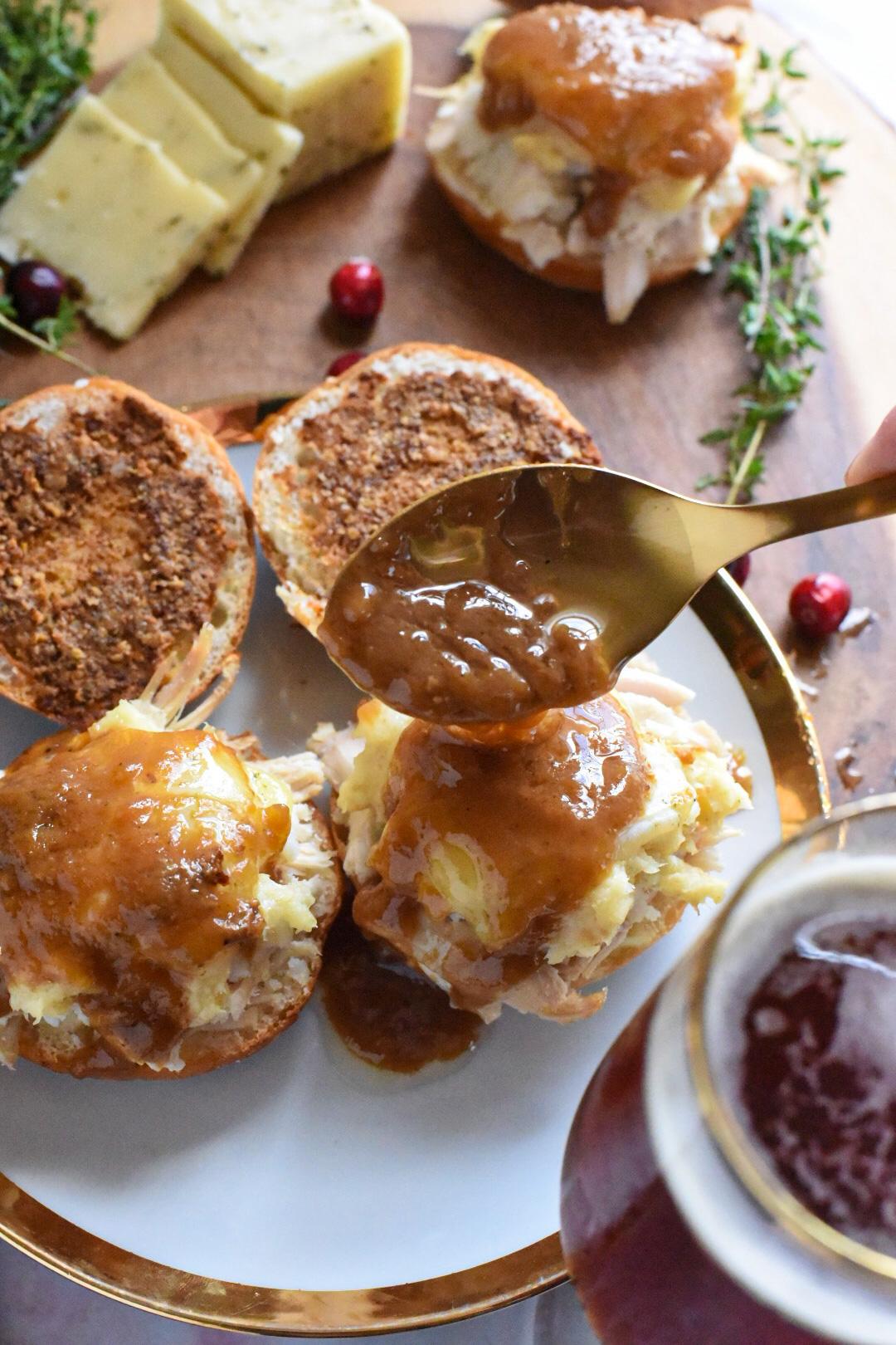 A gold spoon pouring gravy over turkey sliders on a gold rimmed plate.