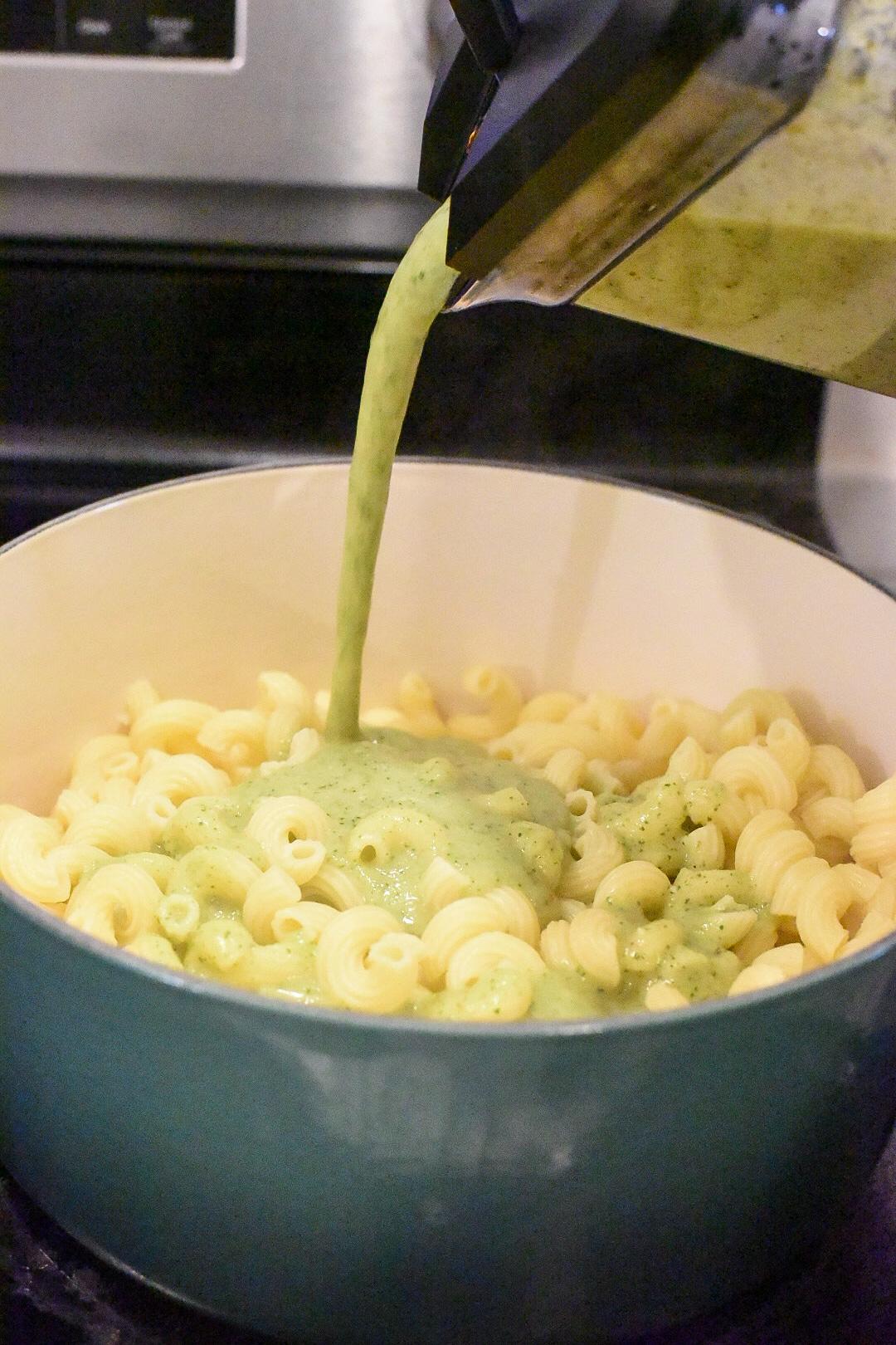A bowl filled with curly pasta with zucchini mac and cheese being poured over it.