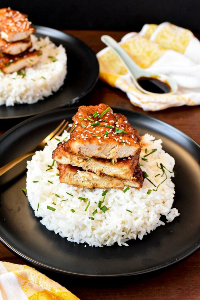 Korean crispy fried chicken breasts stacked on top of white rice on a black plate