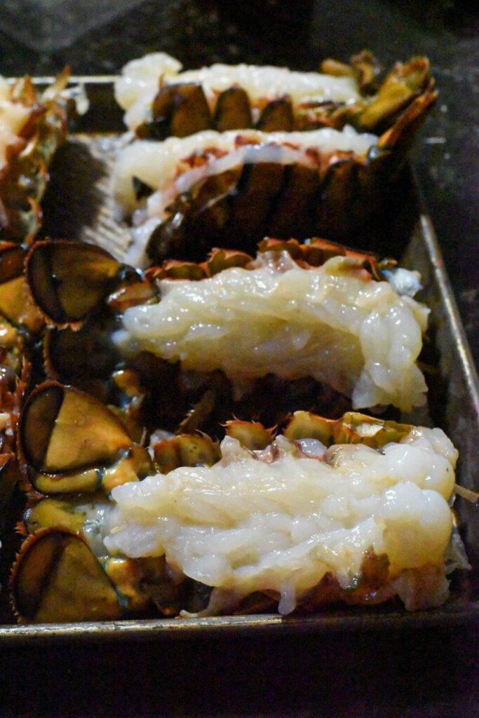 Raw lobster tails cut open on a baking sheet