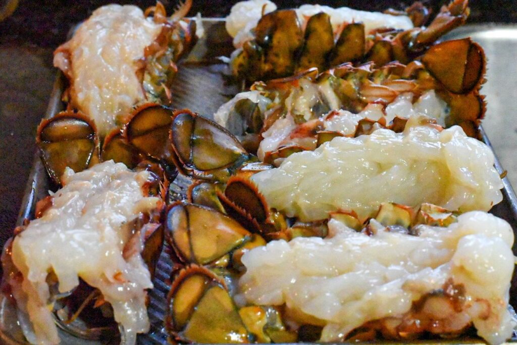 Raw butterflied lobster tails on a baking sheet
