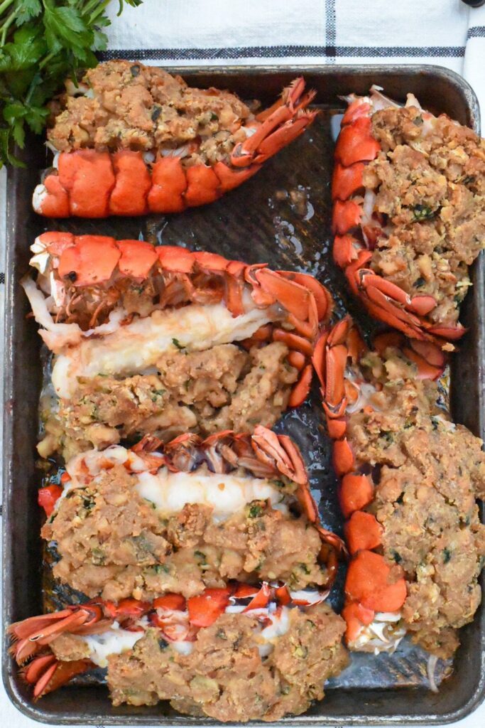 Six baked stuffed lobster tails on a baking sheet