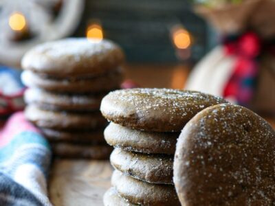 Two stacks of soft gingerspap cookies sprinkled with sugar on a wooden board with christmas lights behind