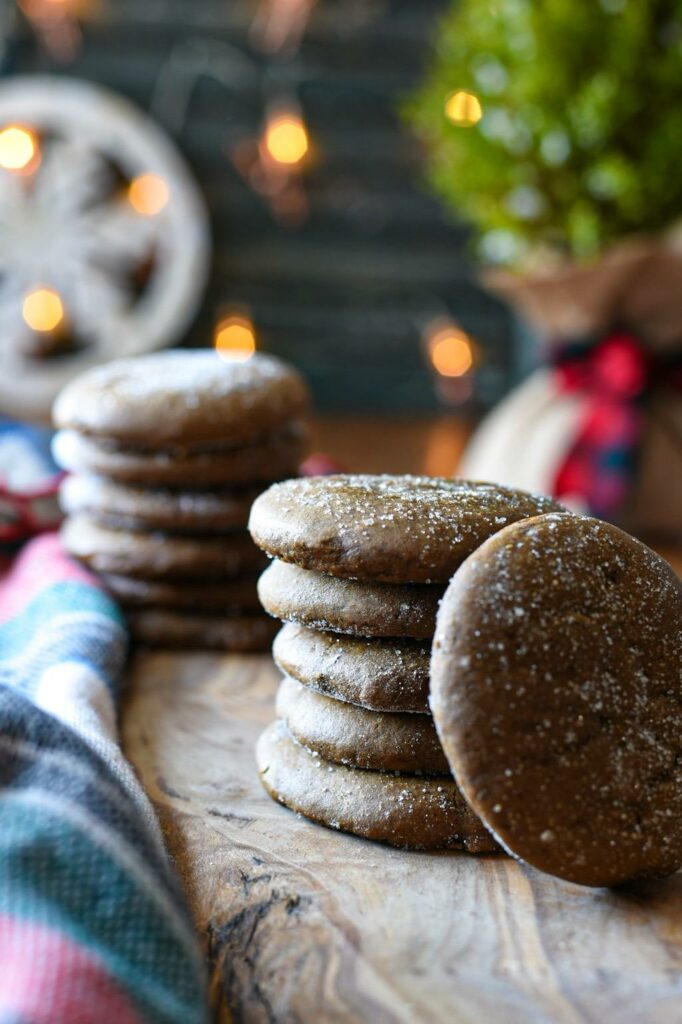 Two stacks of soft gingerspap cookies sprinkled with sugar on a wooden board with christmas lights behind