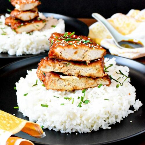 A stack of three sliced fried chicken breasts on white rice with parsley sprinkled over the top