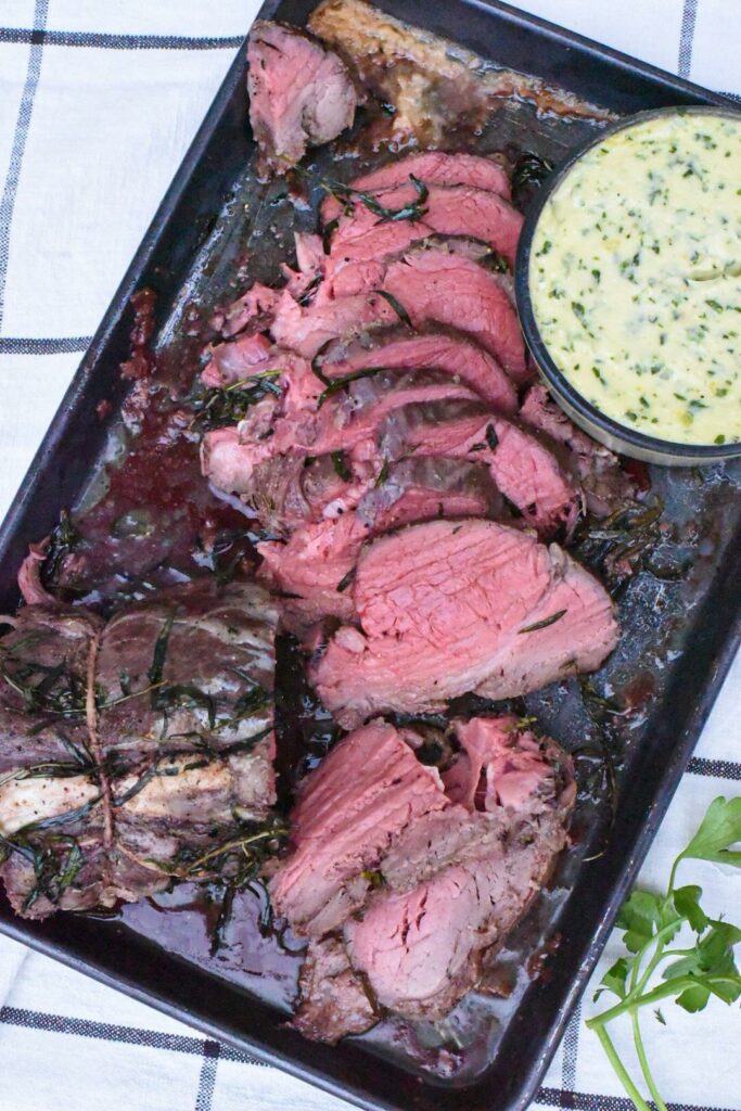 Sliced rare beef tenderloin on a baking sheet with a sauce next to it.