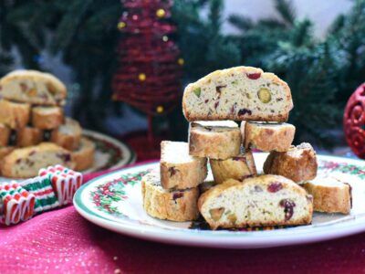Easy Christmas biscotti stacked on a white plate with Christmas decorations behind them.