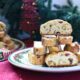 Easy Christmas biscotti stacked on a white plate with Christmas decorations behind them.