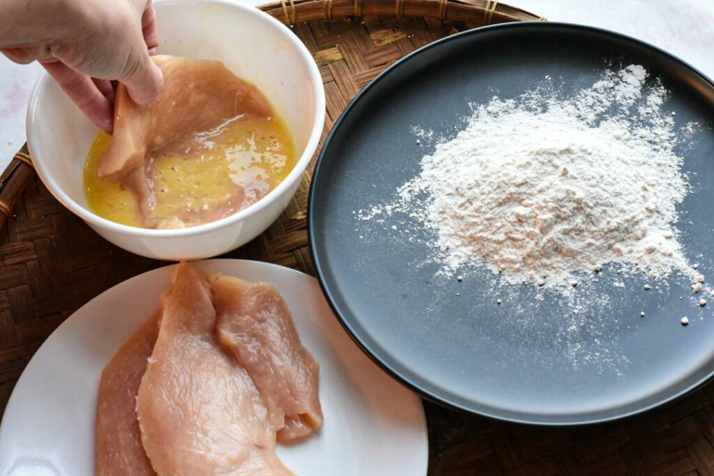 Dipping raw chicken in egg with a plate full of flour next to it