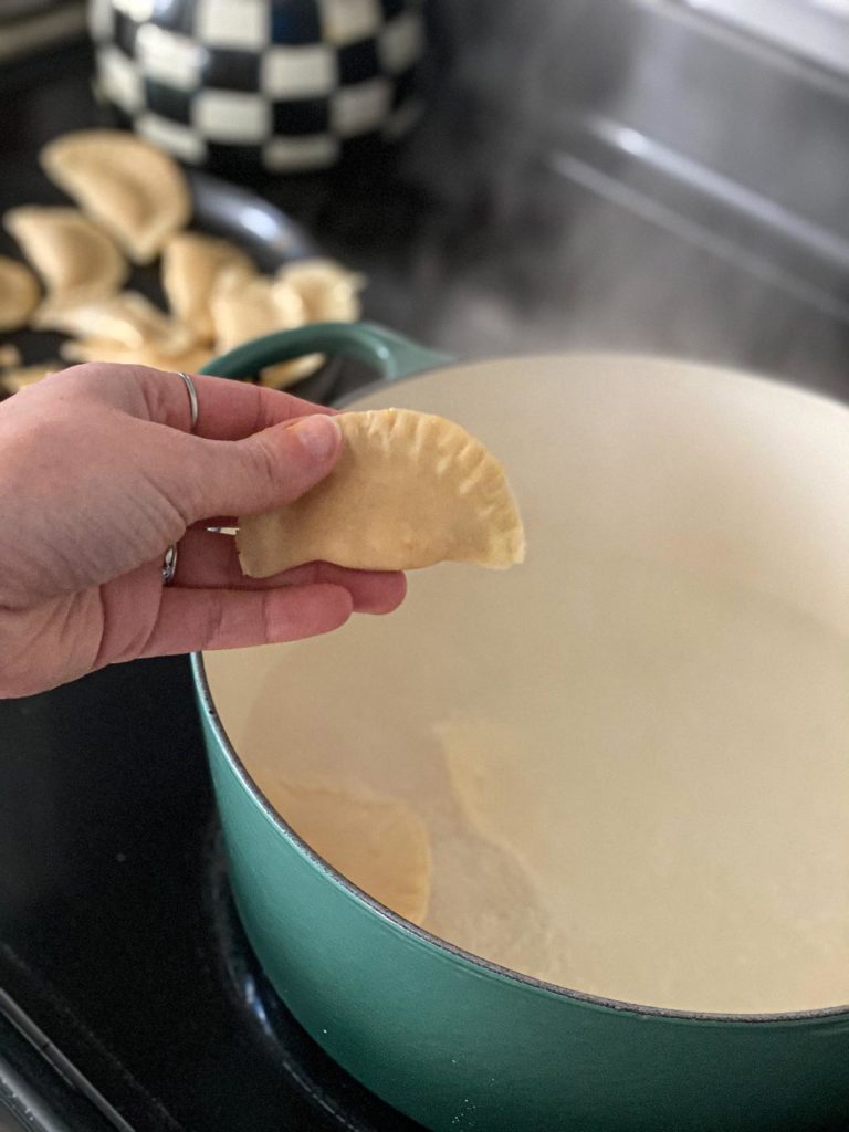 A hand holding a buffalo chicken pierogi over a pot of boiling water