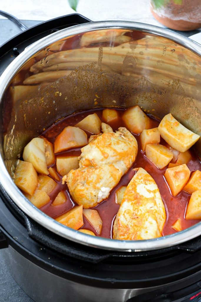 An instant pot filled with cooked chicken breasts, cooked cubed potatoes and bright red buffalo sauce