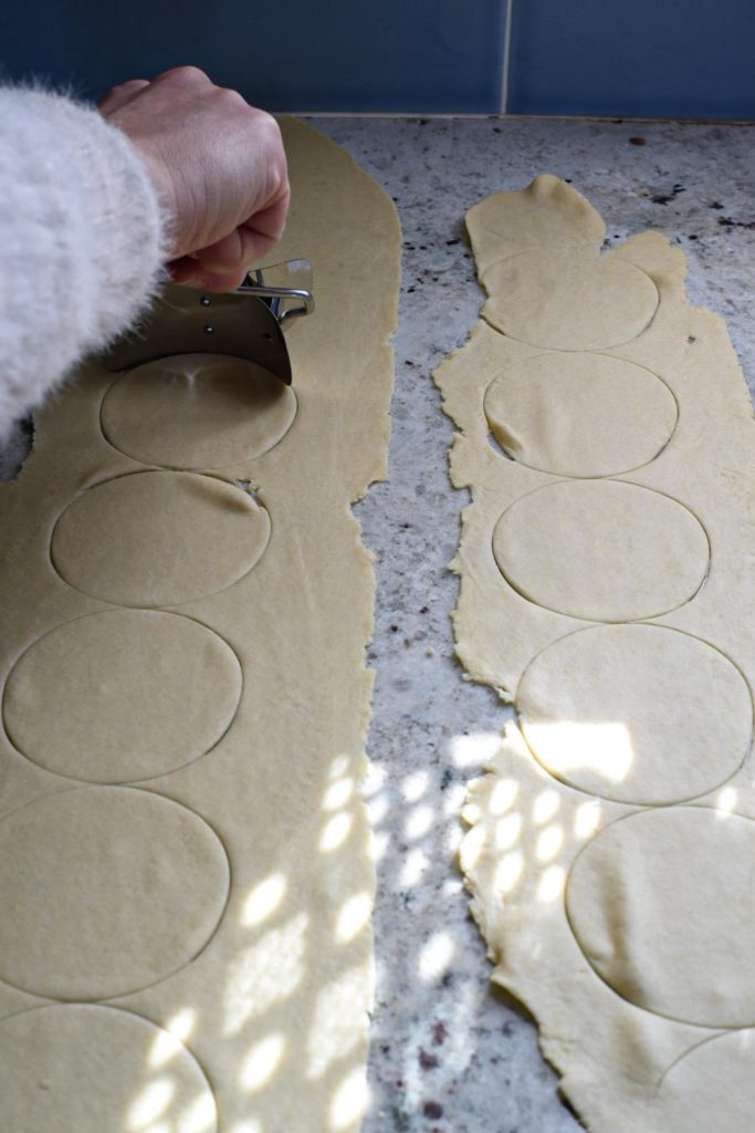 Two flat sheets of dough on a white granite counter with a hand rolling a pierogi maker over the dough to make even circles
