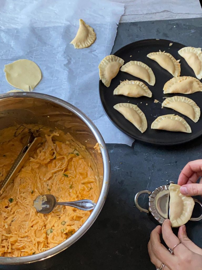 Hands making buffalo chicken pierogies with an instant pot filled with buffalo chicken dip next to it