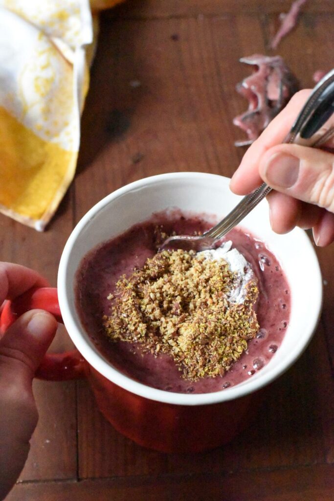 A mug filled with a pink blended cherry mixture being mixed with a spoon.