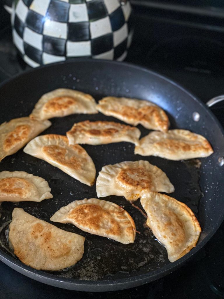 Buffalo chicken pierogies being pan seared in a black pan with a golden brown exterior