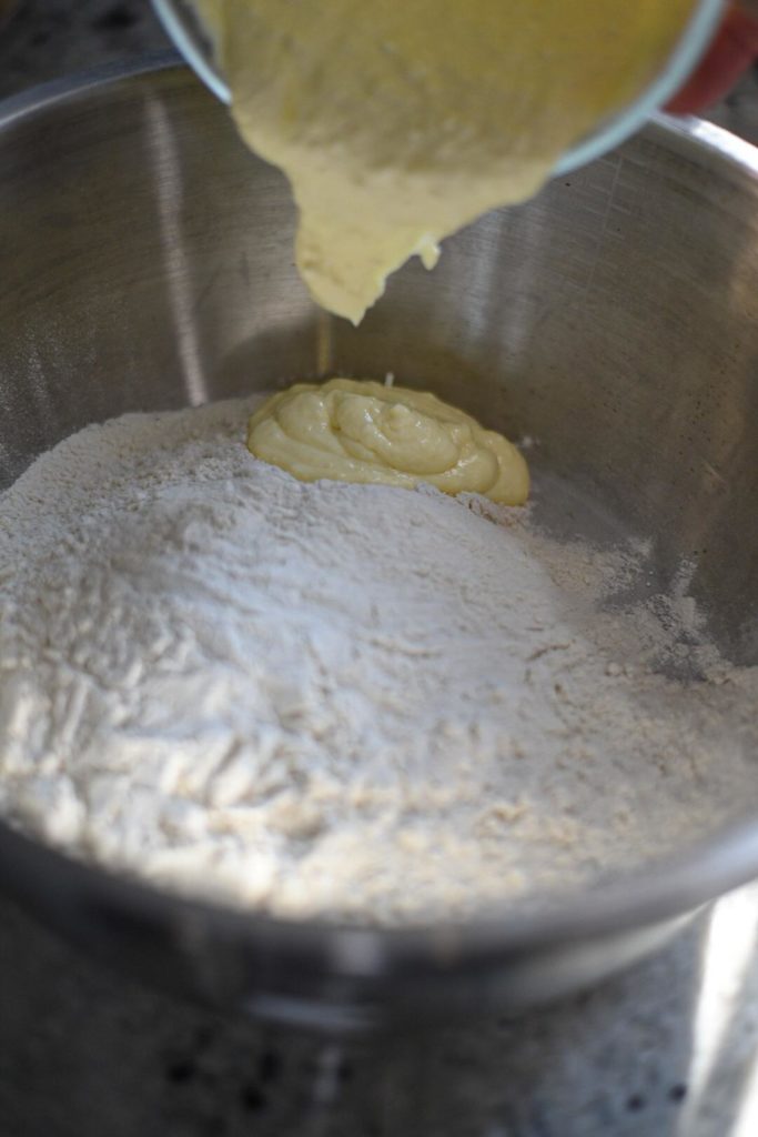 A large bowl fillled with flour with a wet mixture being poured into the bowl