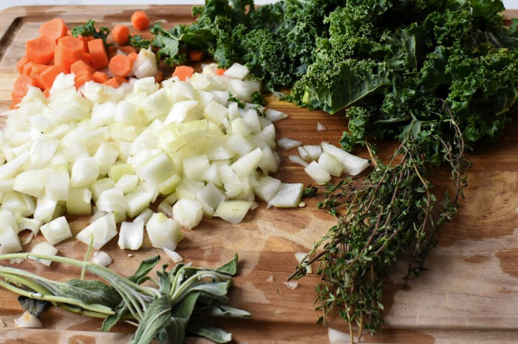 A wooden cutting board filled with kale, chopped onion, carrot and thyme