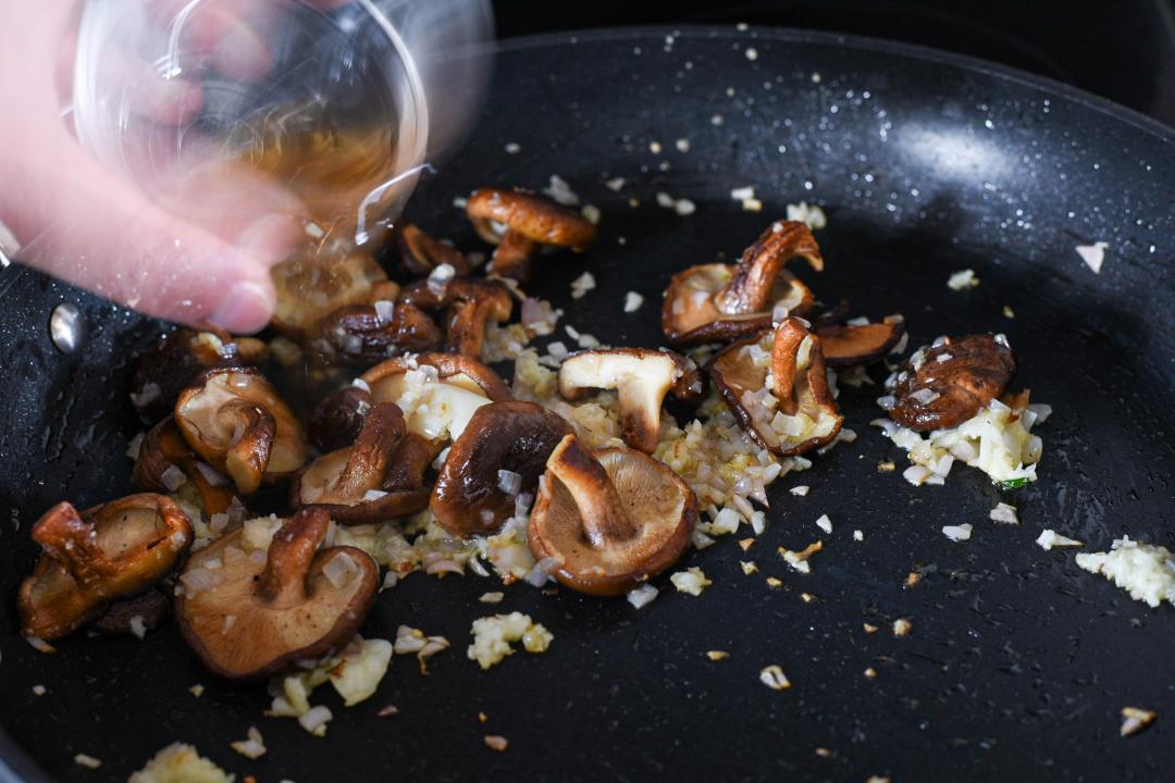 A nonstick pan with a shallot pasta recipe and a hand adding salt.
